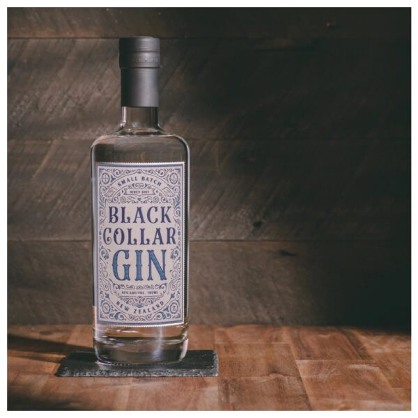 Clear bottle of Black Collar Gin with decorative label on a wooden surface.