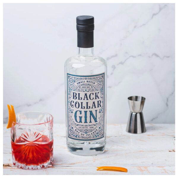 Bottle of Black Collar Gin next to a glass of cocktail and a jigger on a surface.