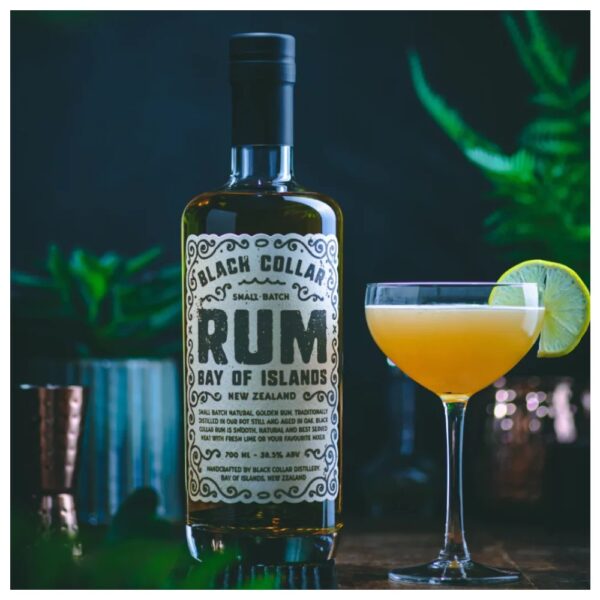 Bottle of Black Collar Distillery Rum with a cocktail glass and lime slice on a dark background.