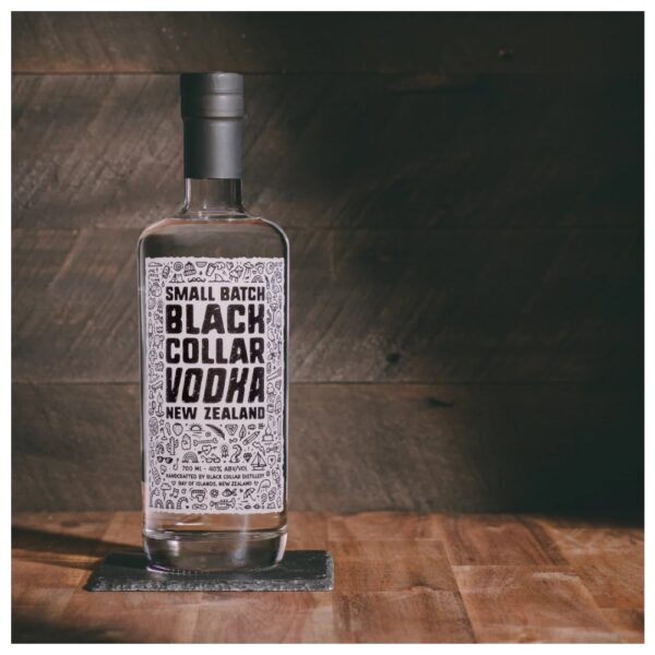 Bottle of Black Collar Distillery vodka with a decorative label, placed on a wooden surface.