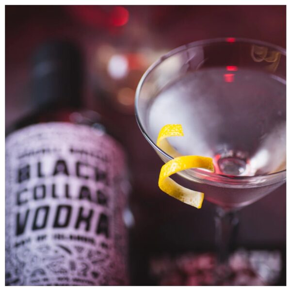 A bottle of Black Collar vodka next to a martini glass garnished with a lemon twist.