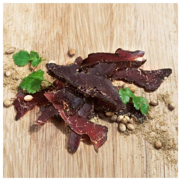 Slices of original biltong arranged on a wooden surface with coriander and spices.