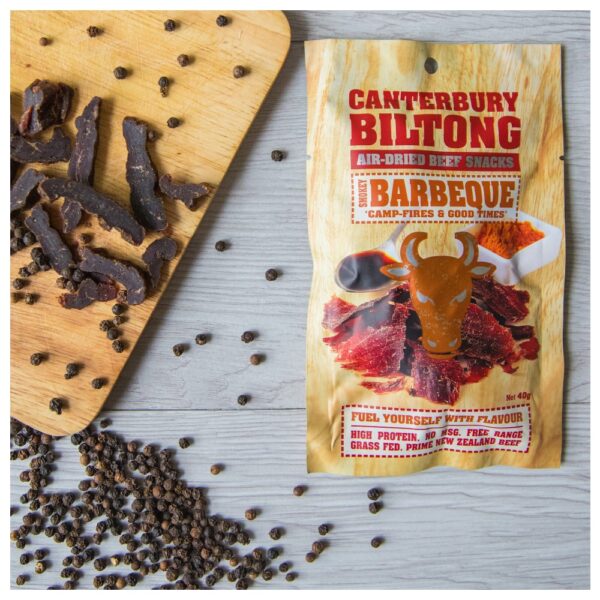 Packaged Canterbury biltong beef snacks with a wooden cutting board and pieces of biltong.