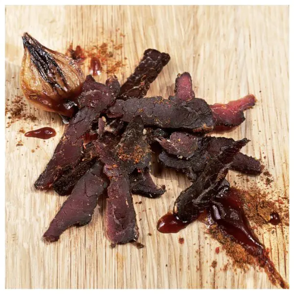 Sliced BBQ flavoured biltong pieces arranged on a wooden surface with a small onion.