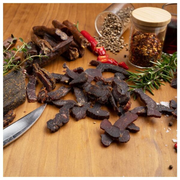 Sliced chilli biltong arranged on a wooden surface with spices and herbs.